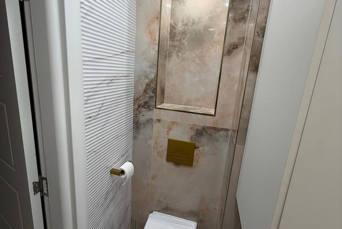 Современный санузел с мраморной отделкой, стильным унитазом и аккуратным освещением. Идеально для покупки недвижимости в Болгарии.