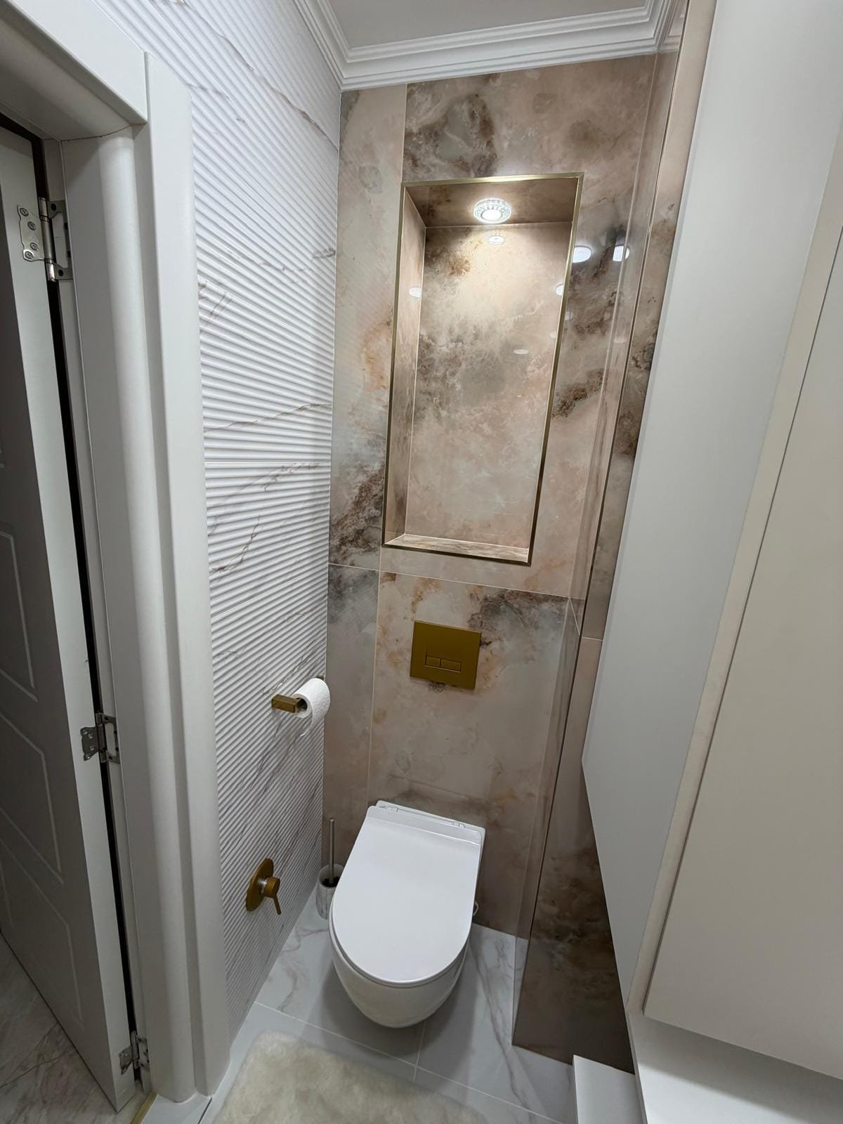 Современный санузел с мраморной отделкой, стильным унитазом и аккуратным освещением. Идеально для покупки недвижимости в Болгарии.