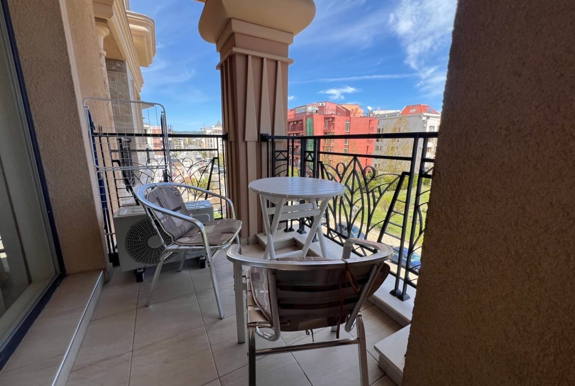 Озеленённый балкон с белым столиком и стульями, overlooking residential район в Болгарии, идеален для отдыха и инвестиций в недвижимость.