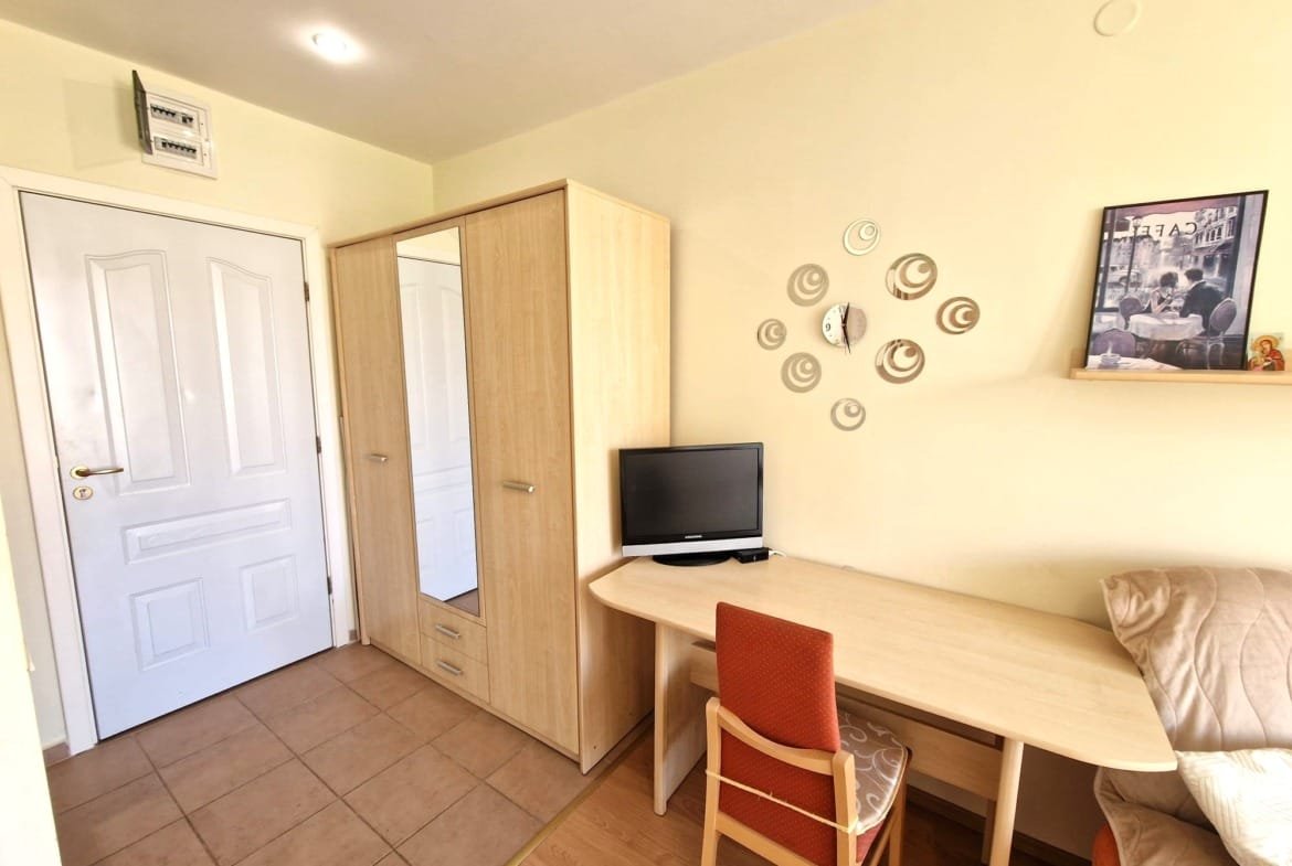 Уютная комната с шкафом, столом, стулом и телевизором, идеальная для проживания в Болгарии.