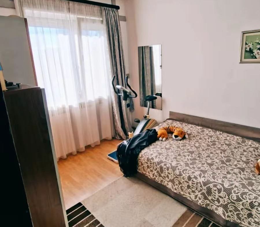 Уютная спальня с прозрачными шторами, двуспальной кроватью и тренажером, идеальна для комфортной жизни в Болгарии.