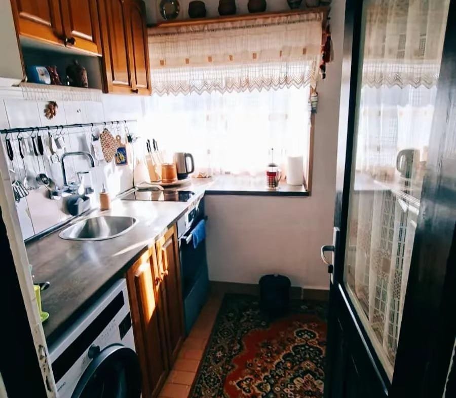 Уютная кухня с деревянными шкафчиками, стиральной машиной, плитой и ярким ковром, идеально подходящая для жизни в Болгарии.