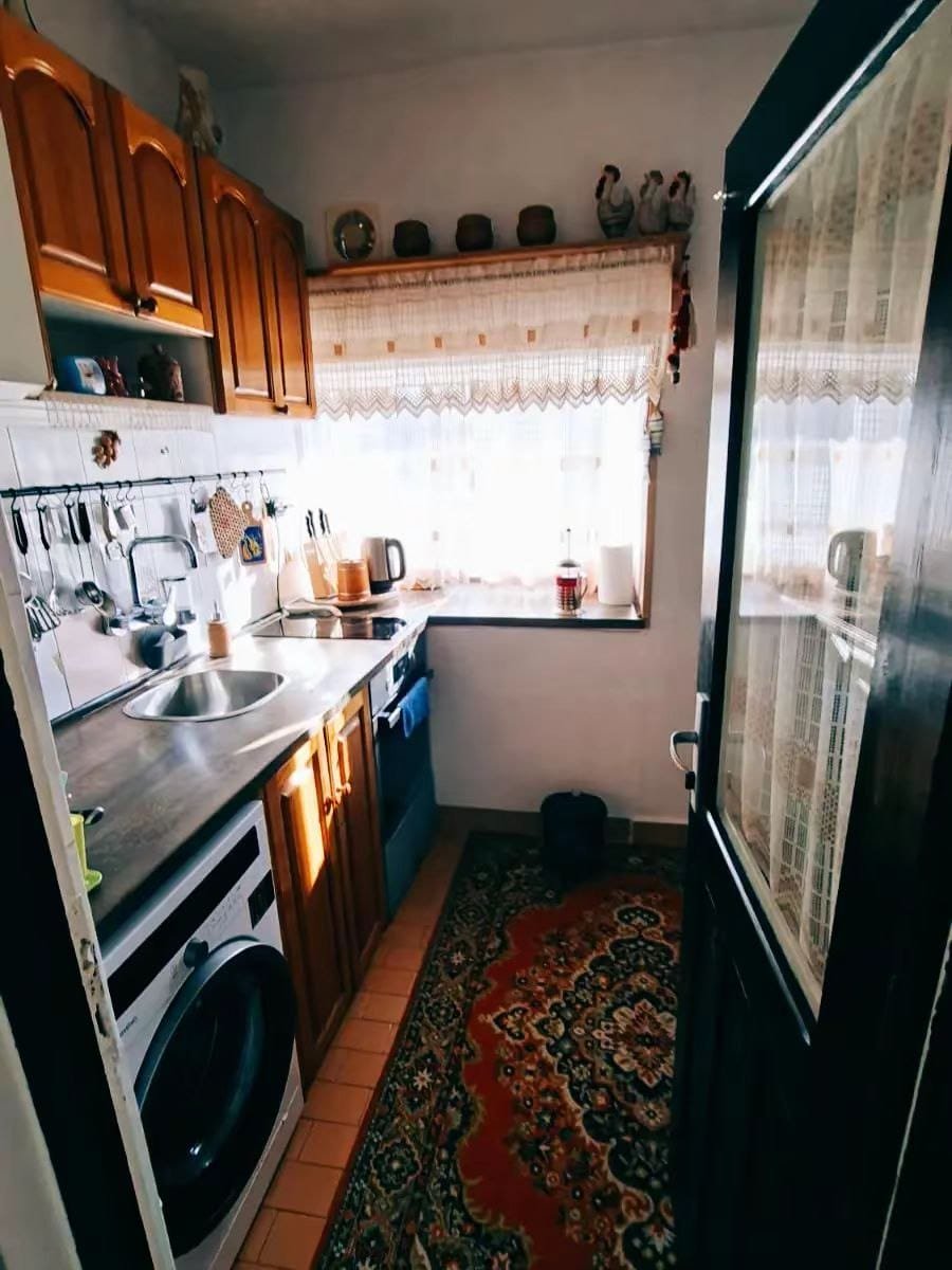 Уютная кухня с деревянными шкафчиками, стиральной машиной, плитой и ярким ковром, идеально подходящая для жизни в Болгарии.