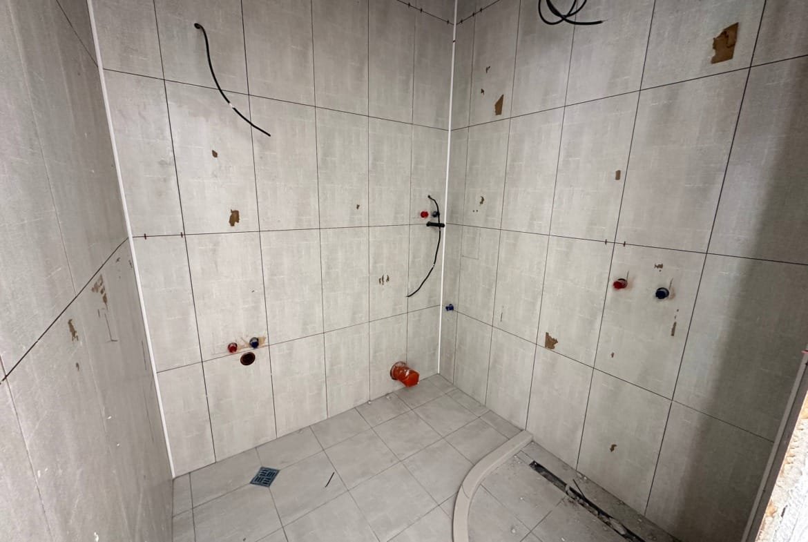 ПустаяBathroom с серыми плитками, без сантехники и отделки, подготовленная для продажи недвижимости в Болгарии.